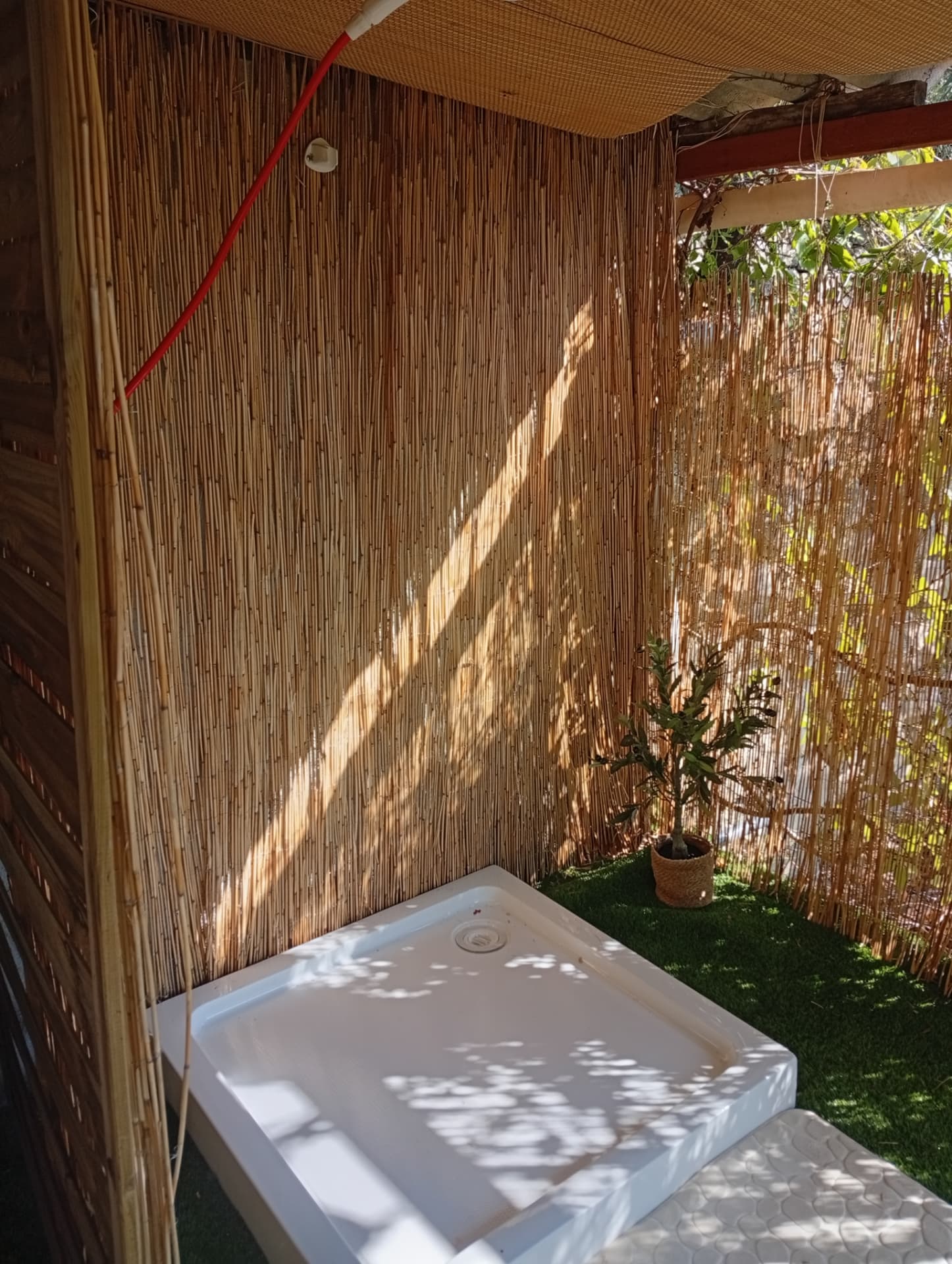 Douche extérieure abritée par des canisses avec receveur blanc